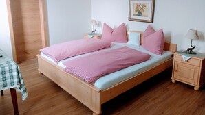 Una cama de madera con ropa de cama a cuadros rosas, una mesita de noche con una lámpara y un cuadro en la pared.