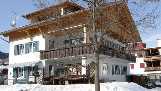 Un edificio de dos pisos con un balcón, una terraza de madera y suelo cubierto de nieve.