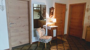 Un pasillo con puerta de madera, una silla, una mesita con lámpara y un espejo.