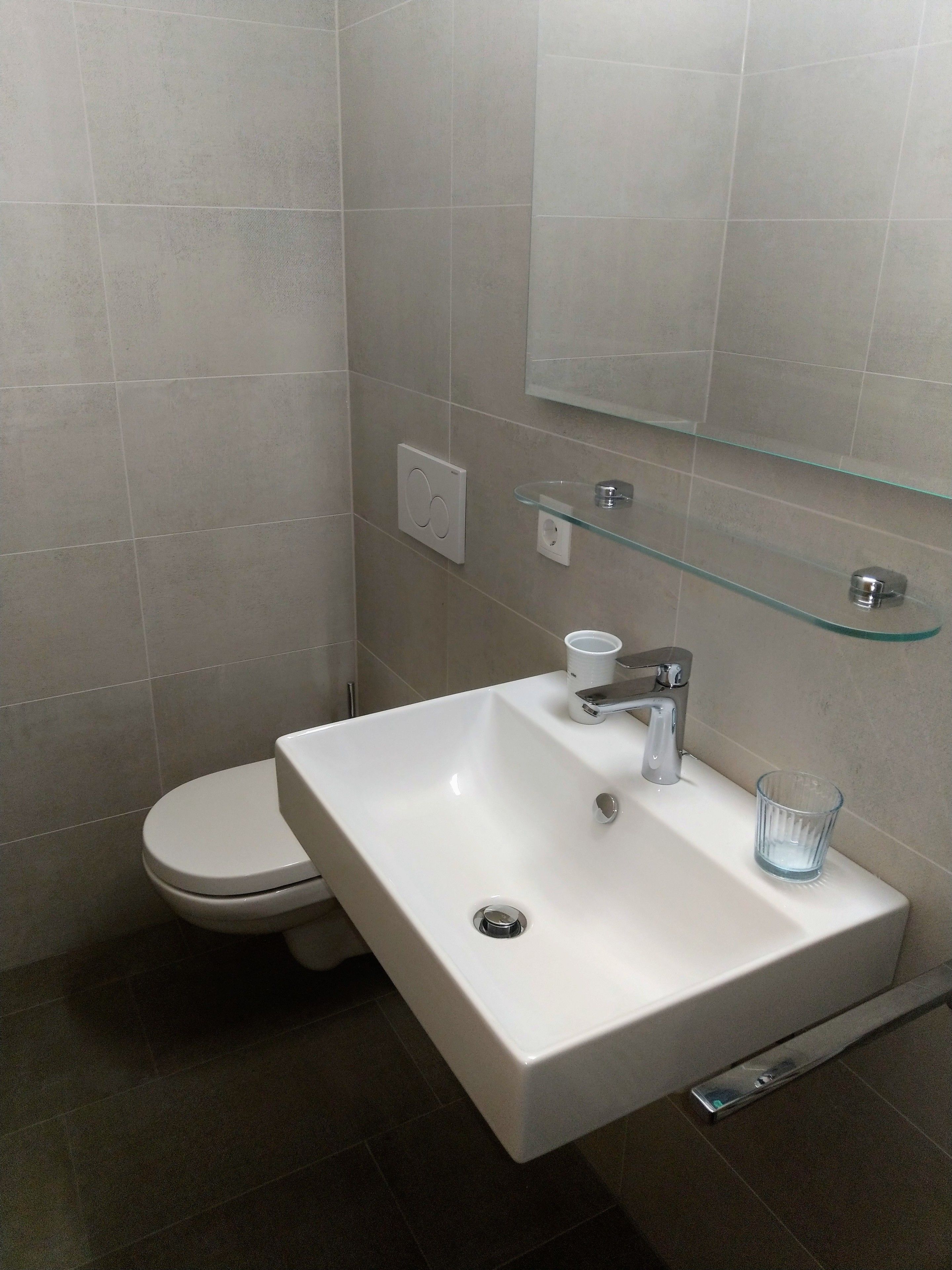 A modern bathroom with a white sink, a glass shelf, and a toilet.