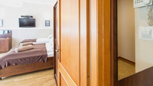 Une chambre d’hôtel avec une armoire en bois, un lit recouvert d’une couverture marron, un téléviseur à écran plat fixé au mur et un téléphone également fixé au mur.