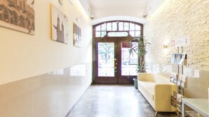 Un couloir avec un mur en pierre, une porte avec des panneaux de verre, une plante en pot et un canapé.