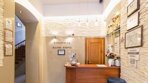 Un espace d’accueil comprenant un comptoir en bois, un bureau de réception, un luminaire fixé au mur, une porte et un sol carrelé.
