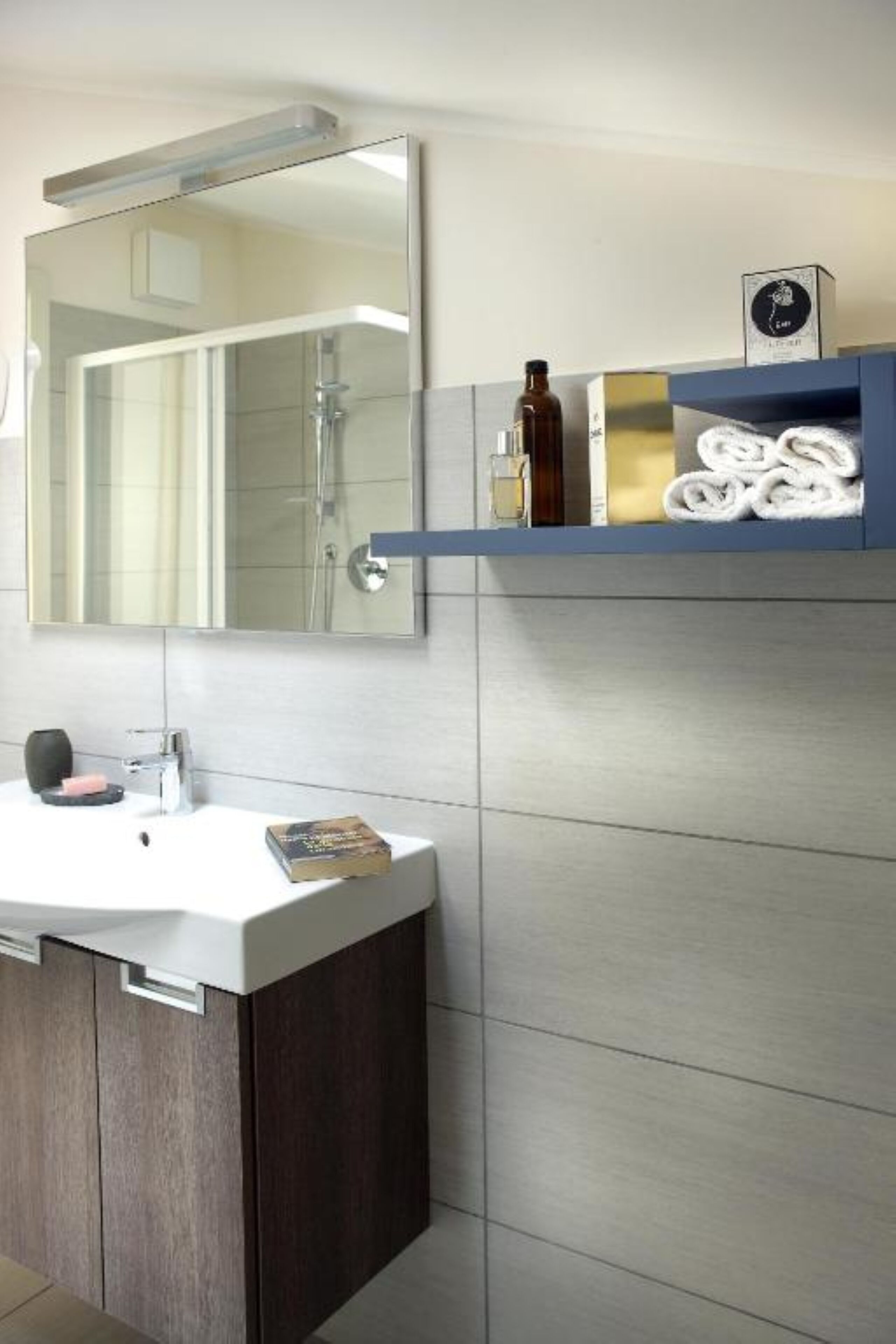 Un baño moderno con un espejo grande, un lavabo blanco, armarios de madera oscura y un estante para toallas.