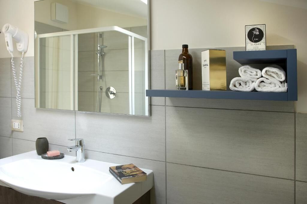 Une salle de bain avec un lavabo blanc, un sèche-cheveux, un miroir, un porte-serviettes avec des serviettes, une bouteille et un livre.