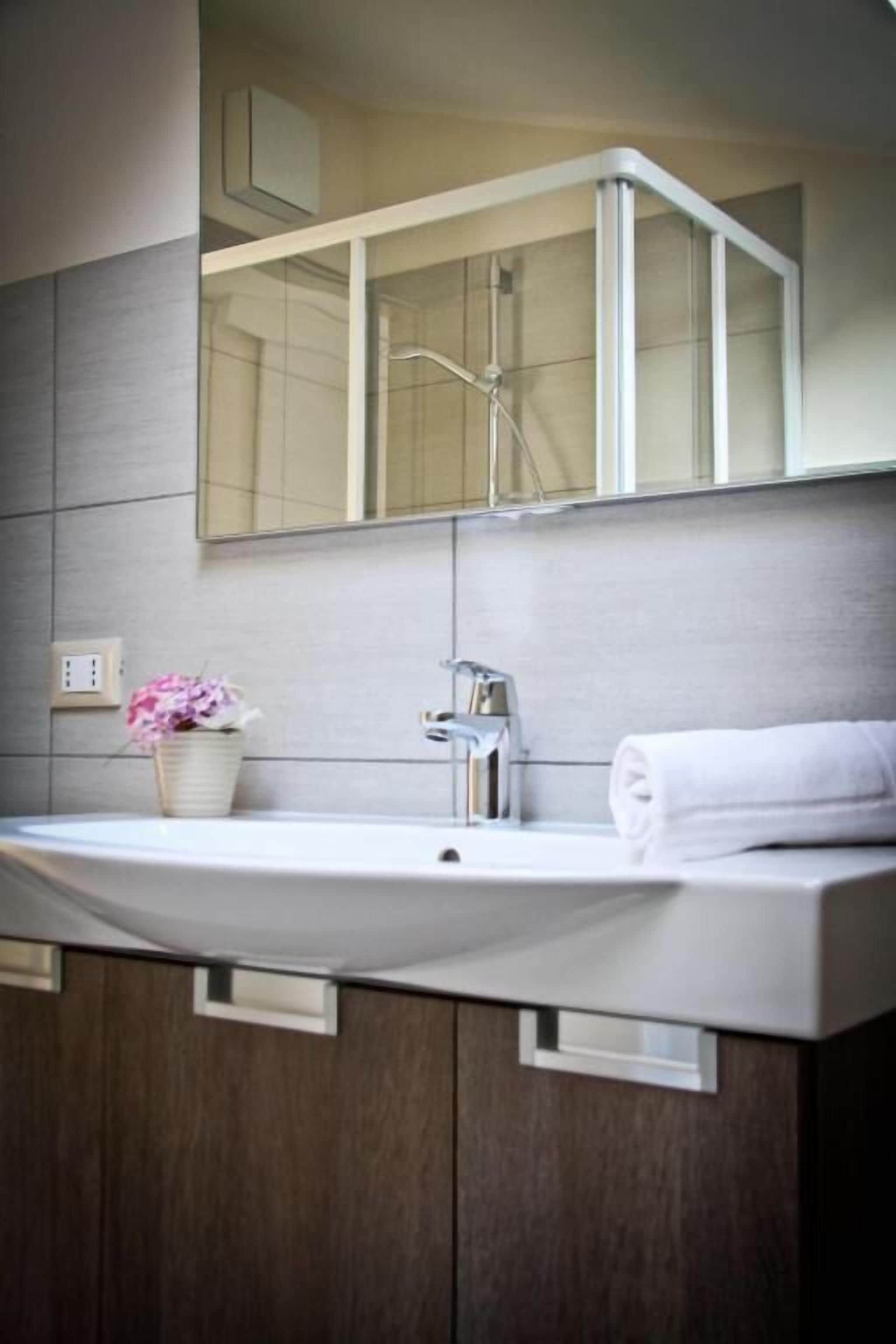 A modern bathroom with a large mirror, a white sink, and a towel on the counter.