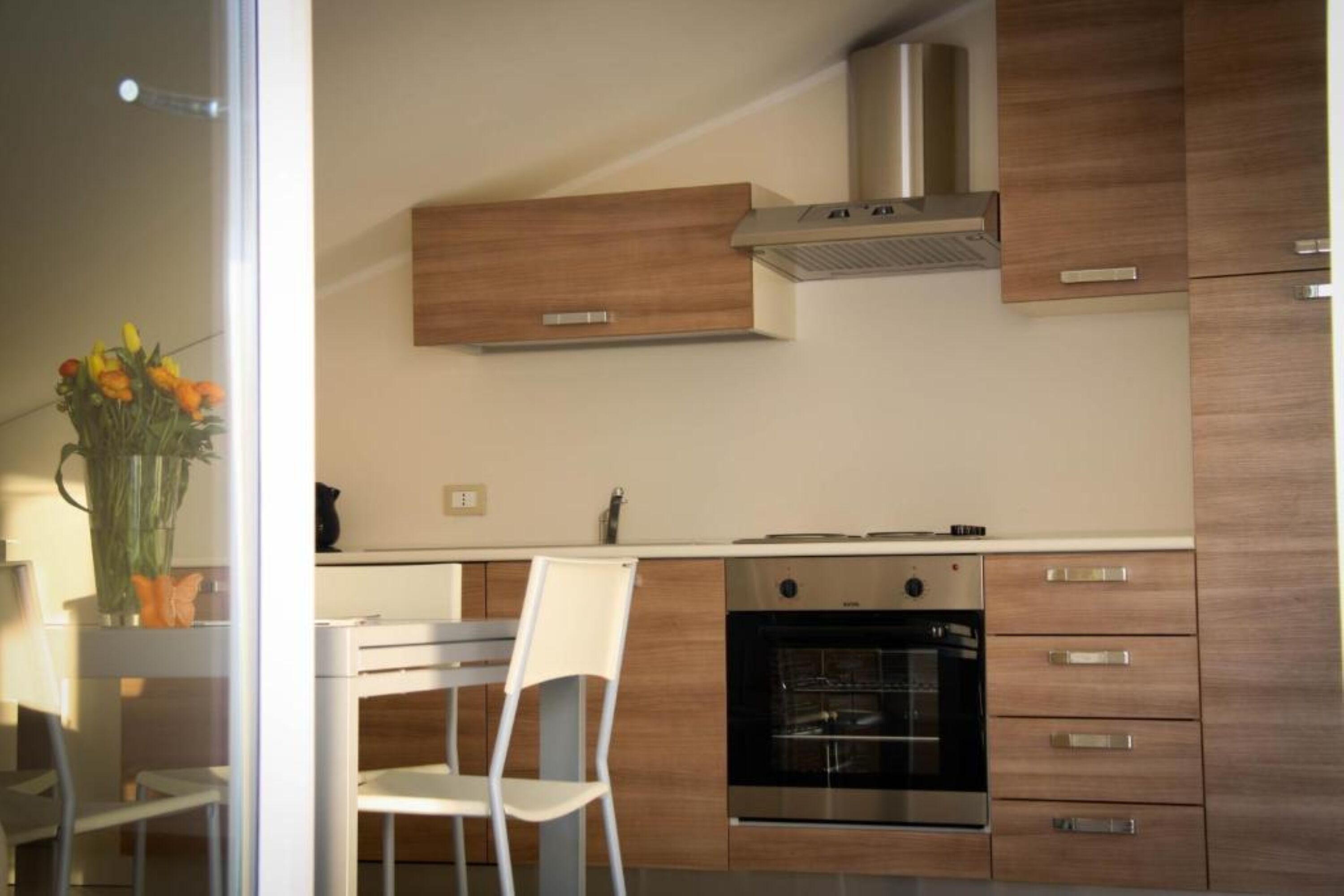 Una cocina moderna con armarios de madera, un horno de acero inoxidable y una silla blanca.