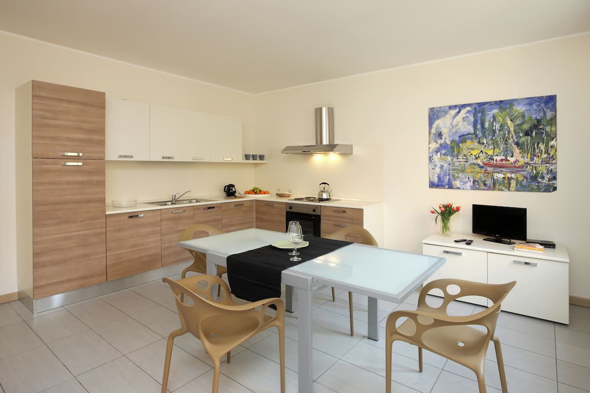 A modern kitchen with a dining area, white cabinets, a stainless steel range hood, and a painting on the wall.