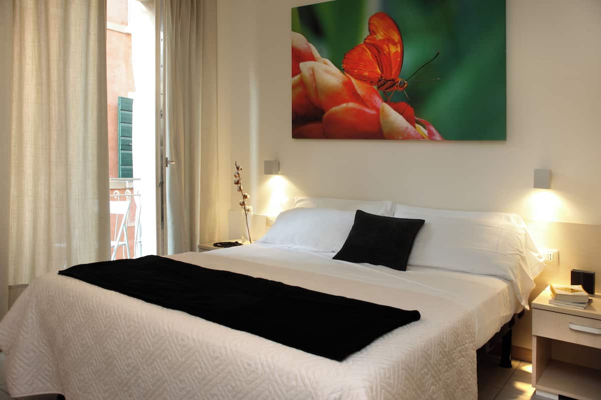 A neatly made bed with a black throw, white bedding, and a painting of a butterfly on the wall.