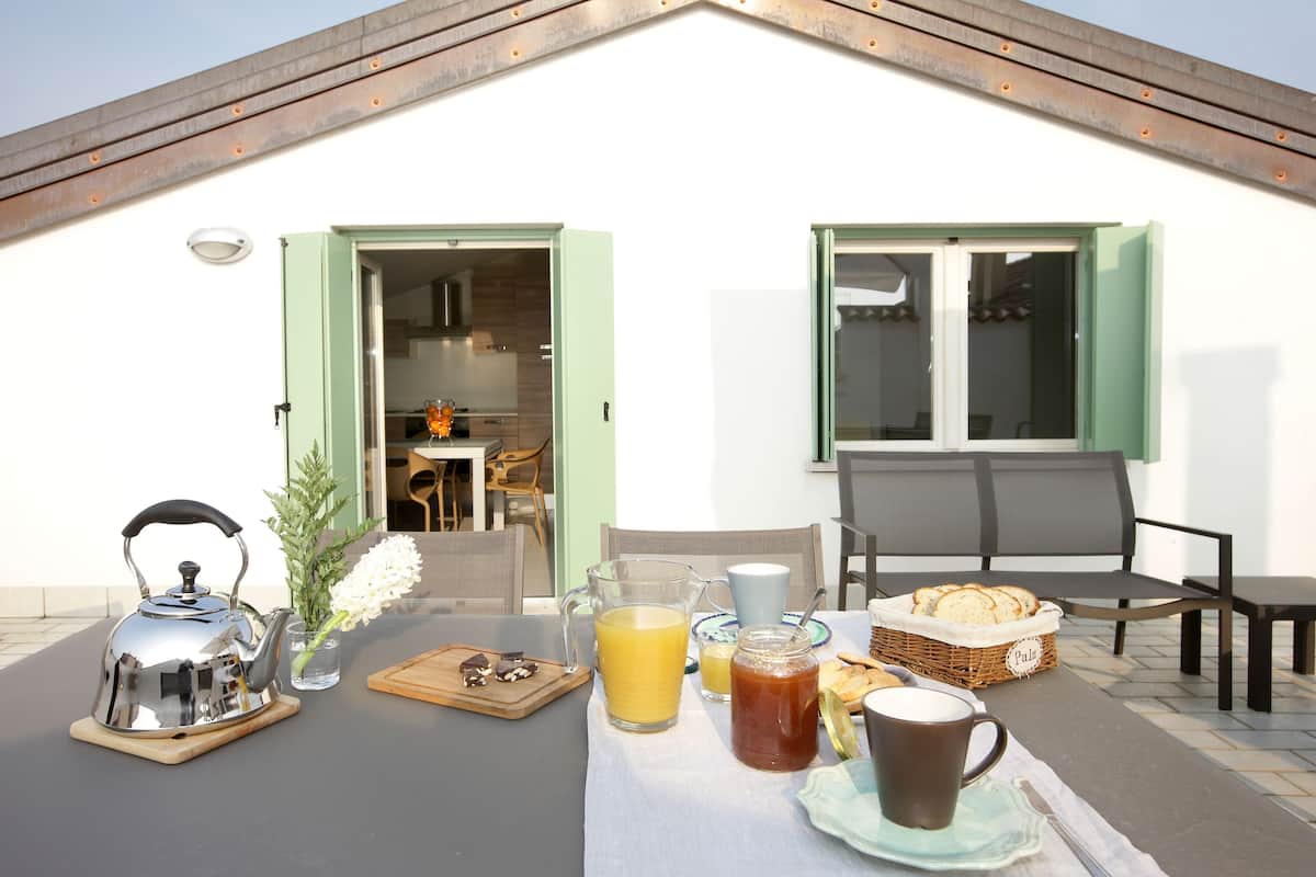 An outdoor breakfast setup with a kettle, tea, juice, and bread on a table.