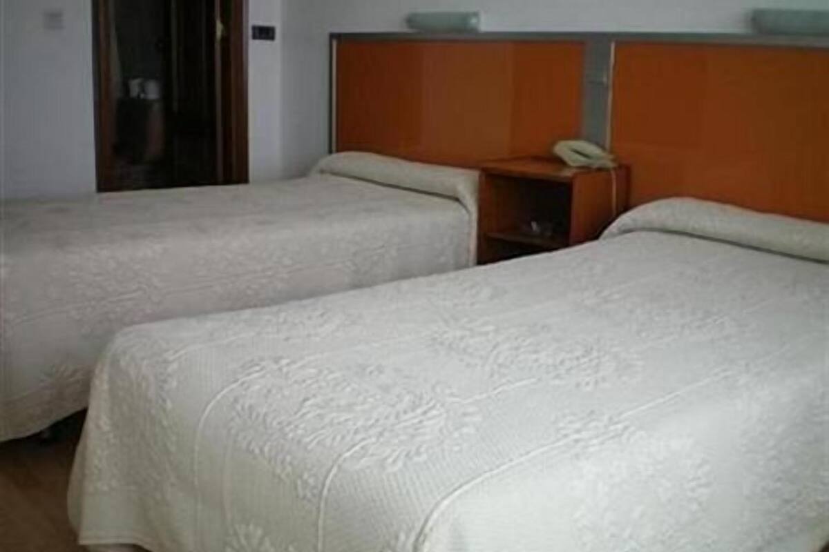 Duas camas de solteiro com cabeceiras, uma mesa de cabeceira com telefone e uma pequena prateleira.