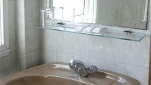 Une salle de bain avec un lavabo beige, une étagère en verre au-dessus et un miroir qui reflète la fenêtre.