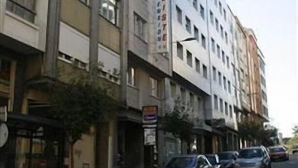 Un immeuble à plusieurs étages, avec une rangée de voitures garées devant.