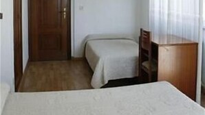 Une petite chambre d’hôtel composée d’une seule pièce, avec un lit, un bureau et une chaise.