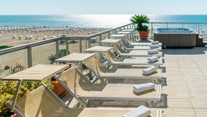 Tagterrasse med liggestole, jacuzzi og udsigt til stranden.