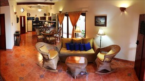 A living room with wicker furniture, a sofa with blue cushions, and a dining area in the background. - Hotel Xalteva (Granada)