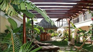 A tropical garden with a thatched-roof structure, lounge chairs, and a stone pathway. - Hotel Xalteva (Granada)