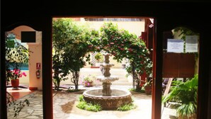 A courtyard with a central fountain, surrounded by potted plants and a stone pathway. - Hotel Xalteva (Granada)