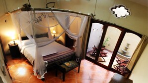 A room with a four-poster bed, a nightstand, a small table, and a view of an outdoor patio area. - Hotel Xalteva (Granada)