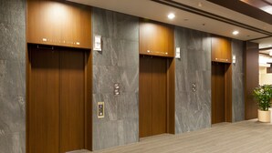 A row of wooden elevator doors with marble walls and a carpeted floor. - Chofu Creston Hotel (Chofu)