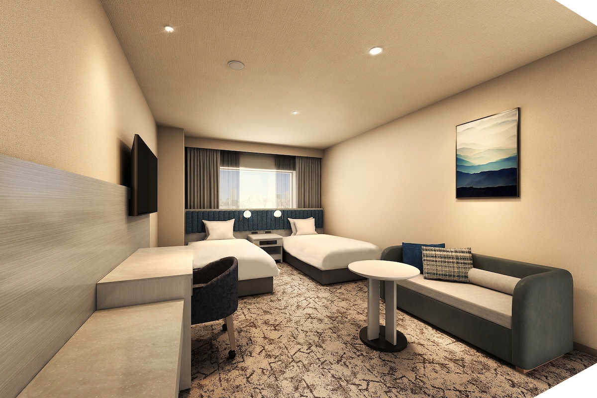 A hotel room with two beds, a sofa, a small table, and a TV mounted on the wall.