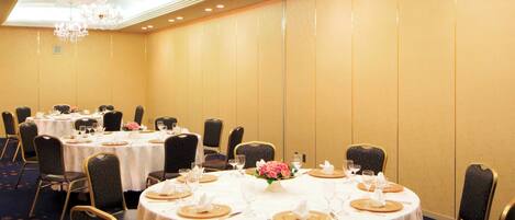 Un salón de banquetes con mesas redondas, sillas, candelabros y piso alfombrado.