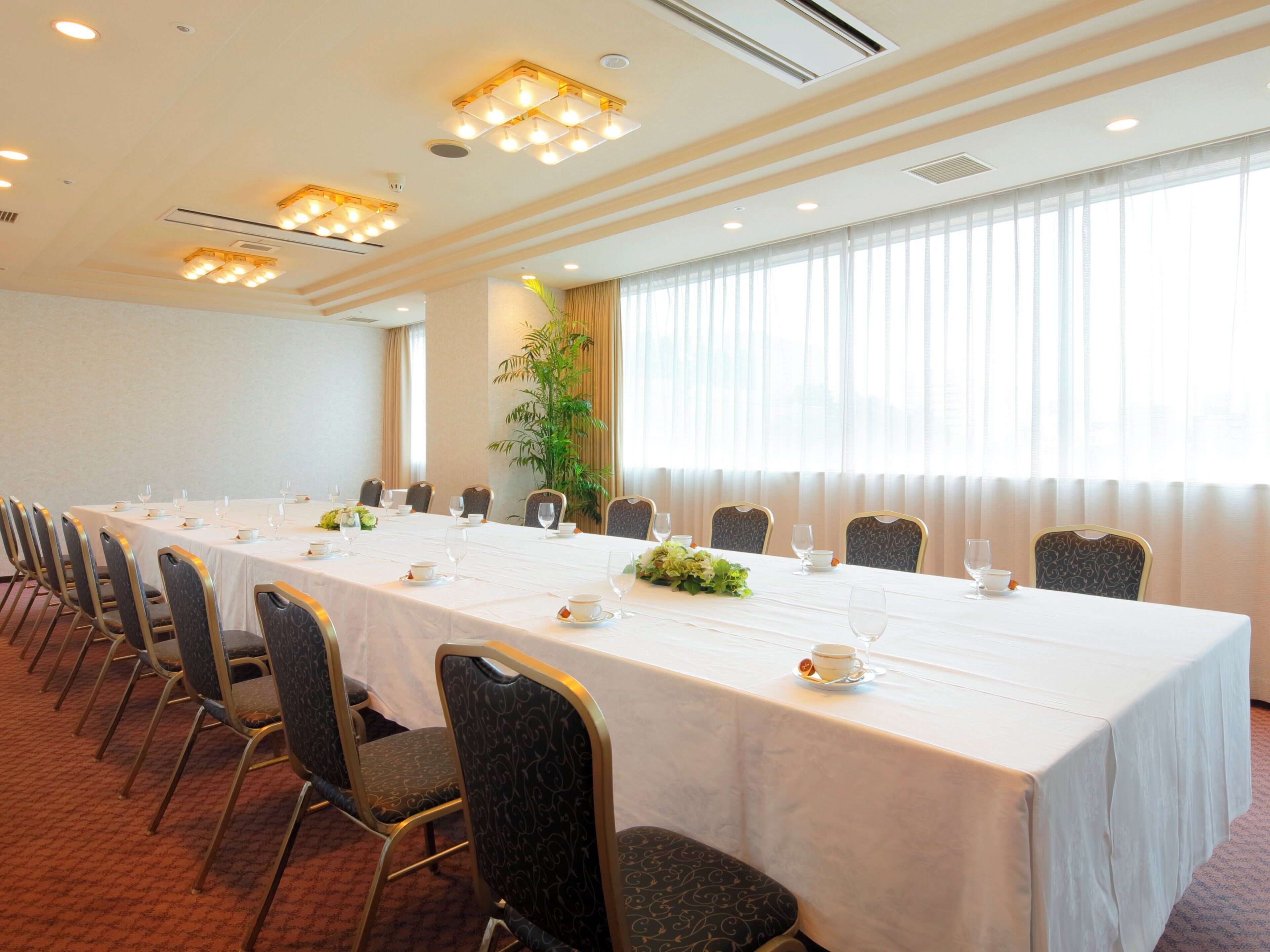 A conference room with a long table, chairs, and a large window with curtains.