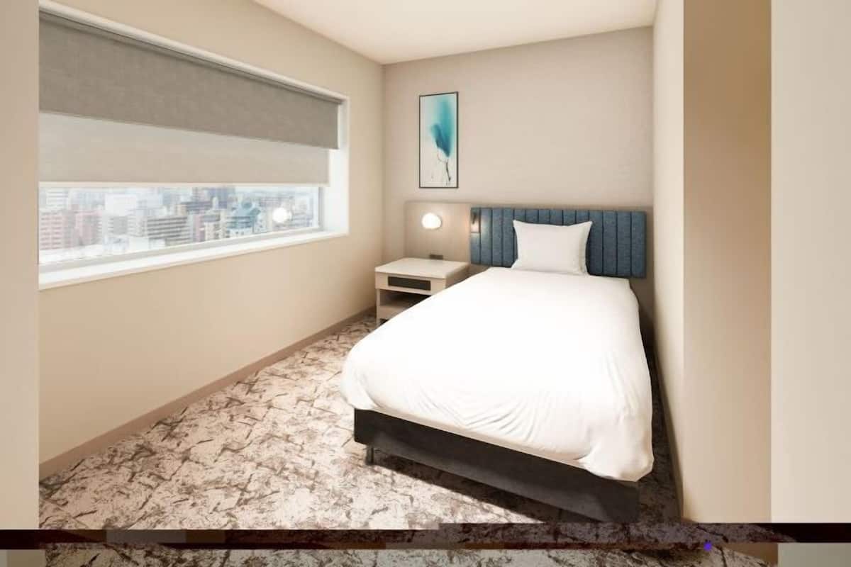 A hotel room with a bed, bedside table, lamp, and a city view through the window.