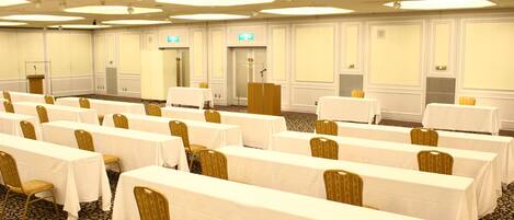 A conference room with rows of tables and chairs, a podium, and a carpeted floor.