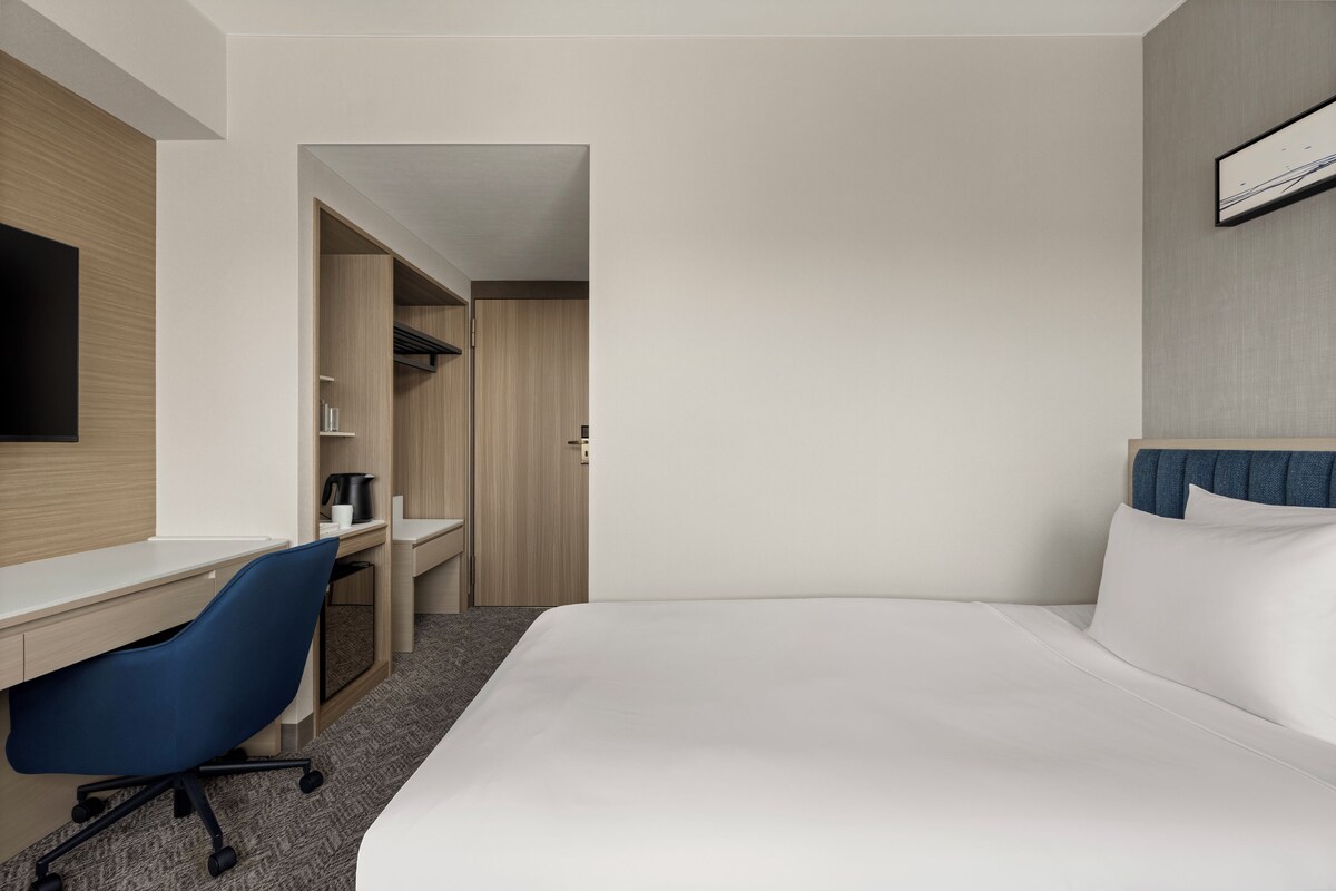A hotel room with a bed, a desk, a chair, a television, and a wardrobe.
