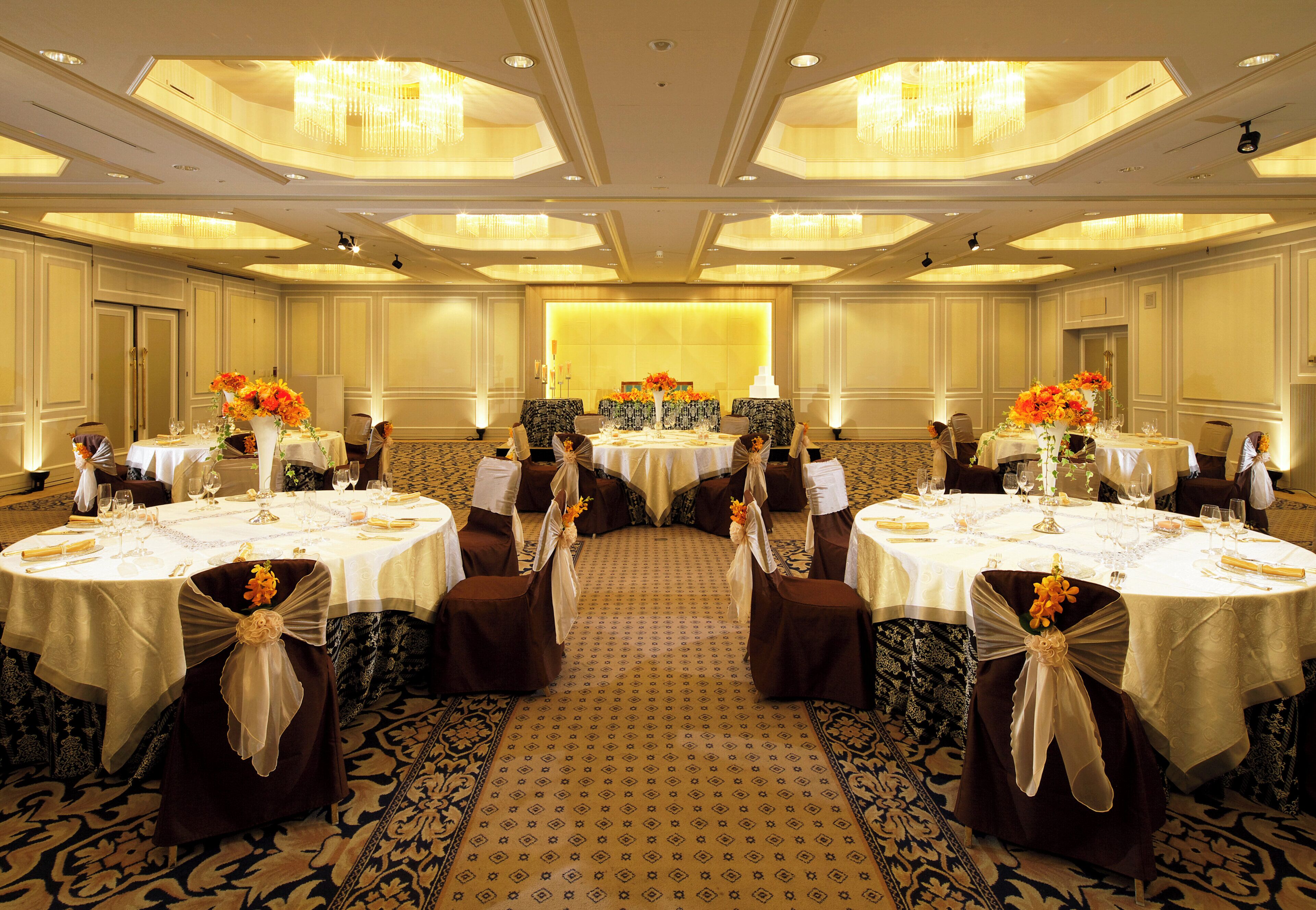 A banquet hall with round tables, chairs, and chandeliers.