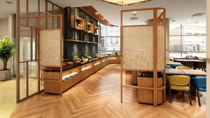A modern interior with wooden flooring, a curved counter with food items, and a seating area with yellow and blue chairs. - Crowne Plaza - ANA Hamamatsu by IHG (Hamamatsu)