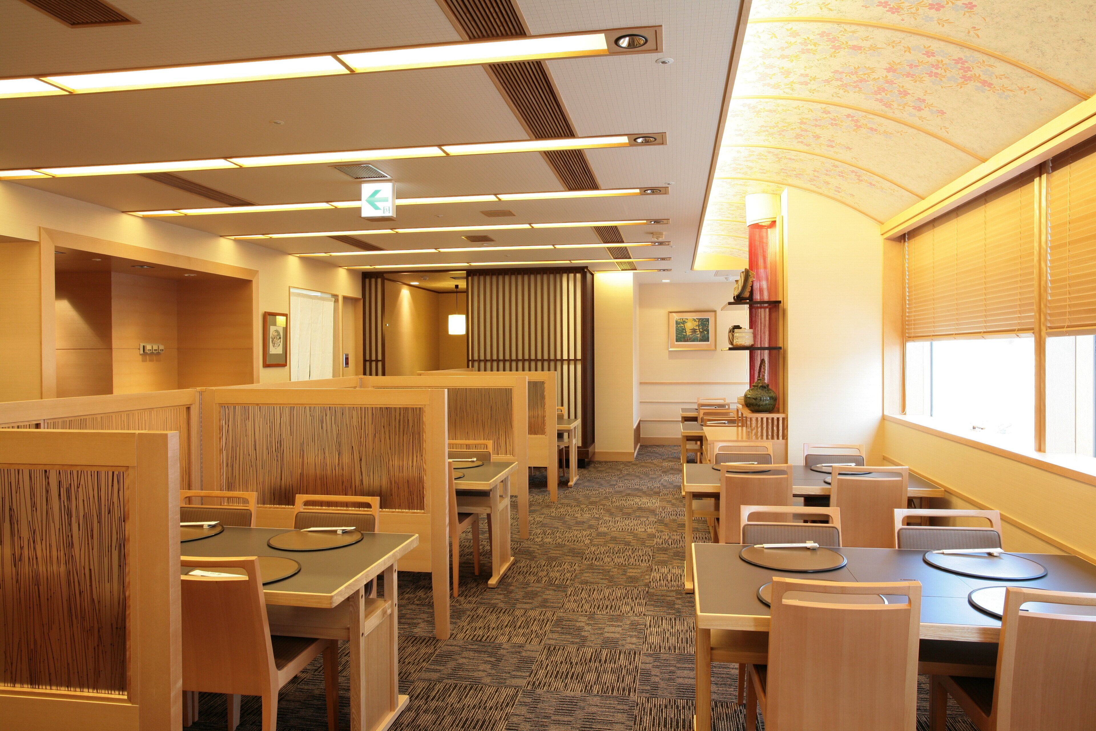A hotel dining area with wooden booths and tables, carpeted flooring, and a ceiling with linear lighting fixtures.