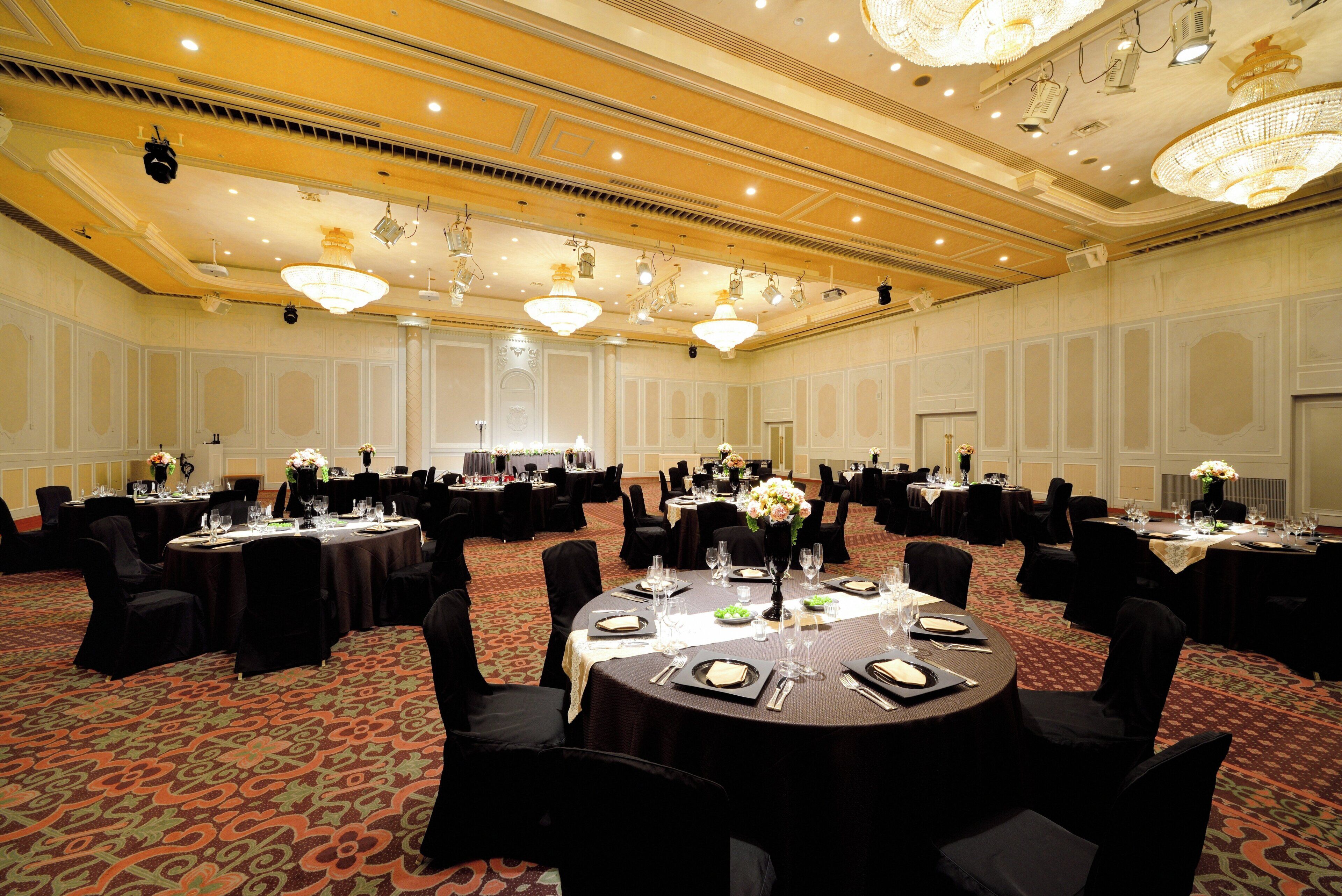 A large conference room with round tables, black chairs, and chandeliers.