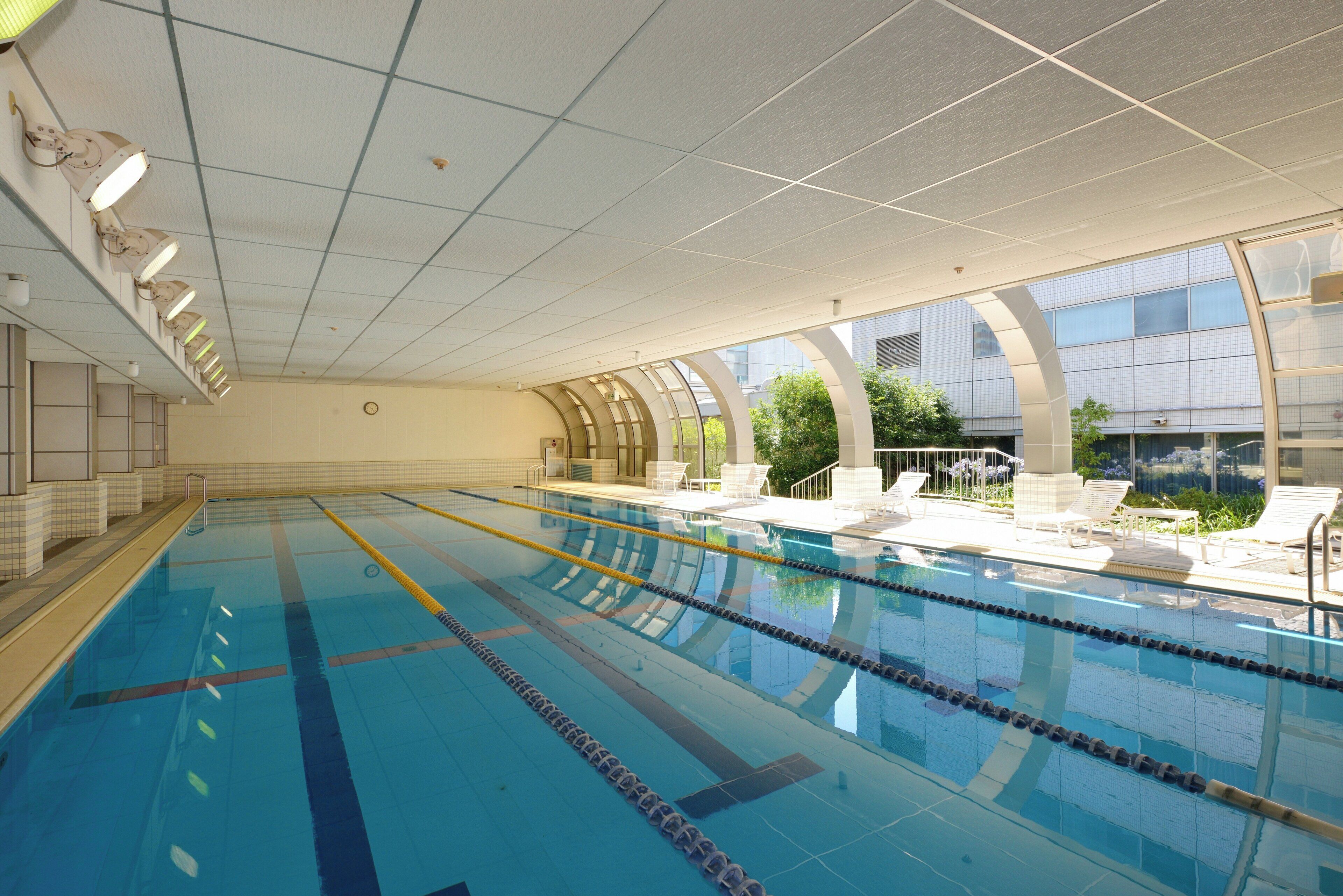A swimming pool with clear lanes, a ceiling with grid pattern, and a view of a building with large windows.