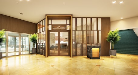 A hotel lobby with a reception desk, glass doors, and a staircase.