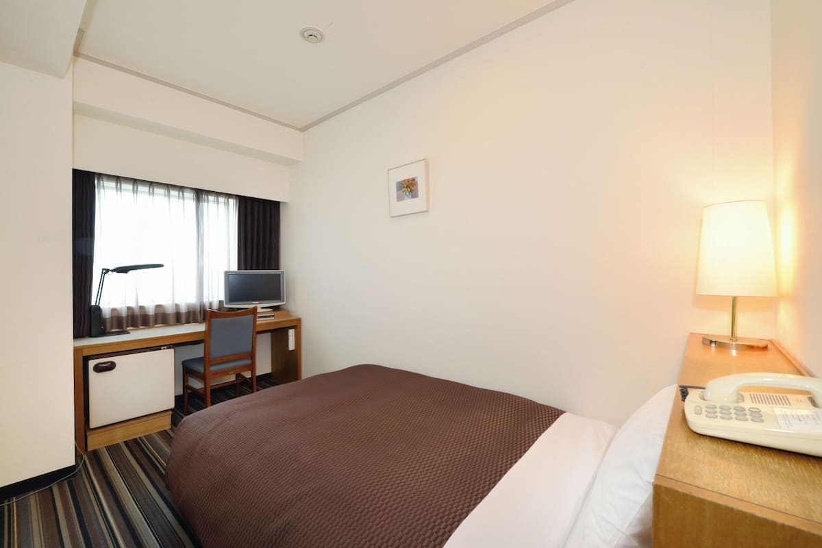 Une chambre d’hôtel équipée d’un lit, d’un bureau avec un ordinateur, d’une chaise, d’un téléphone et d’une lampe.