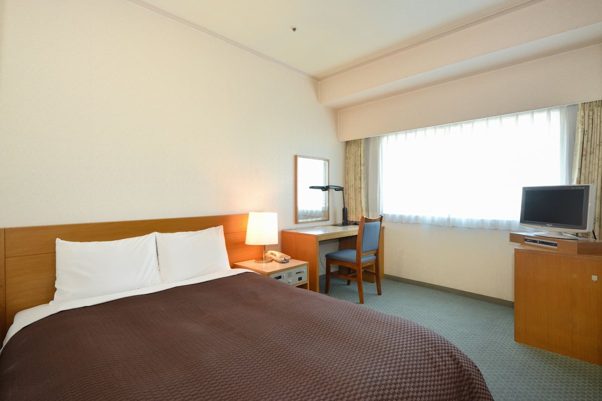 Une chambre d’hôtel avec un grand lit, un bureau avec une chaise, une télévision et une fenêtre avec des rideaux.