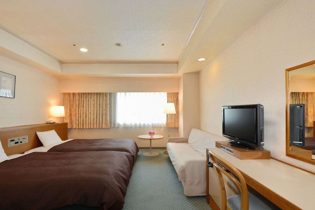 Une chambre d’hôtel avec deux lits, une télévision, un bureau et une chaise.
