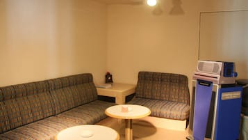 A small, furnished room with a sofa, two round tables, a cabinet, and a cart.