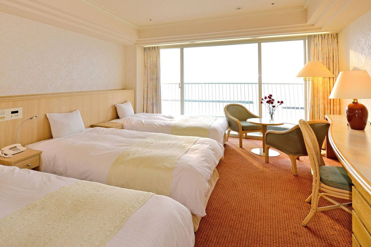 A hotel room with two beds, a desk, a chair, and a large window with a view.