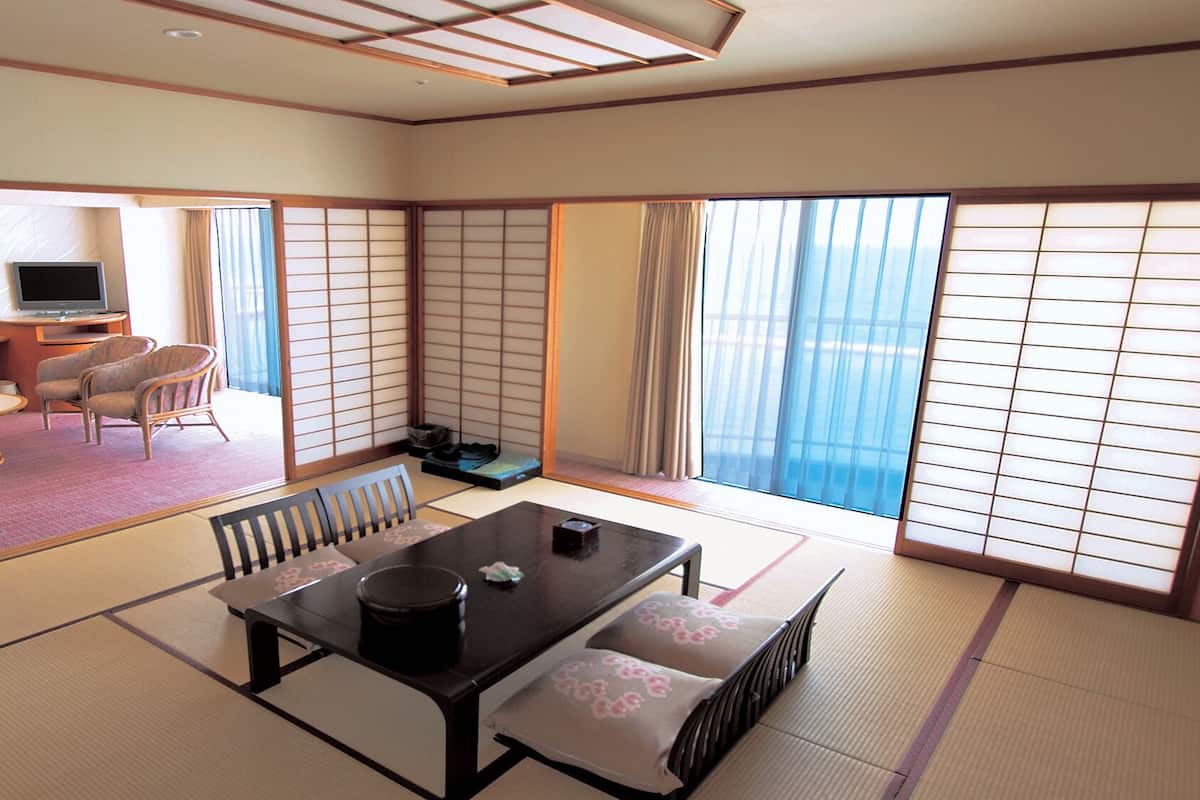 Una habitación japonesa tradicional con suelo de tatami, una mesa baja con cojines, una televisión y vistas al mar.