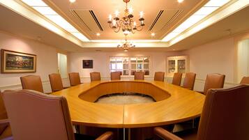 A conference room with a round table, leather chairs, a chandelier, and a painting on the wall.