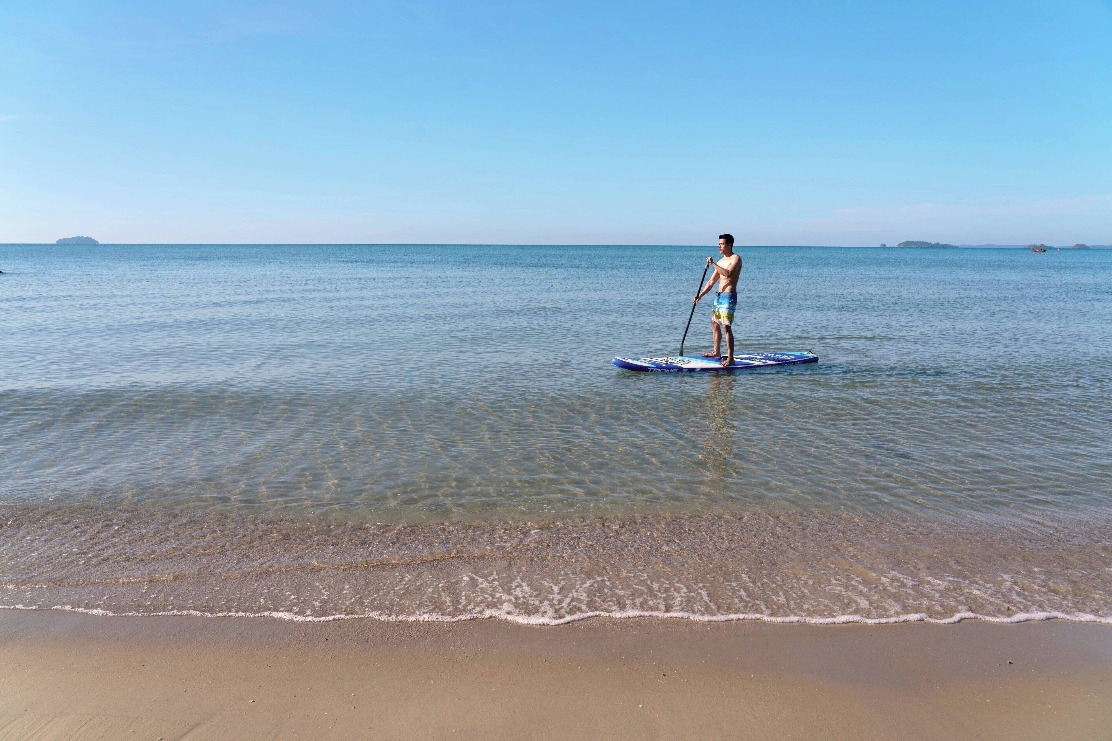 A person paddleboarding on a calm sea with clear skies and distant islands.