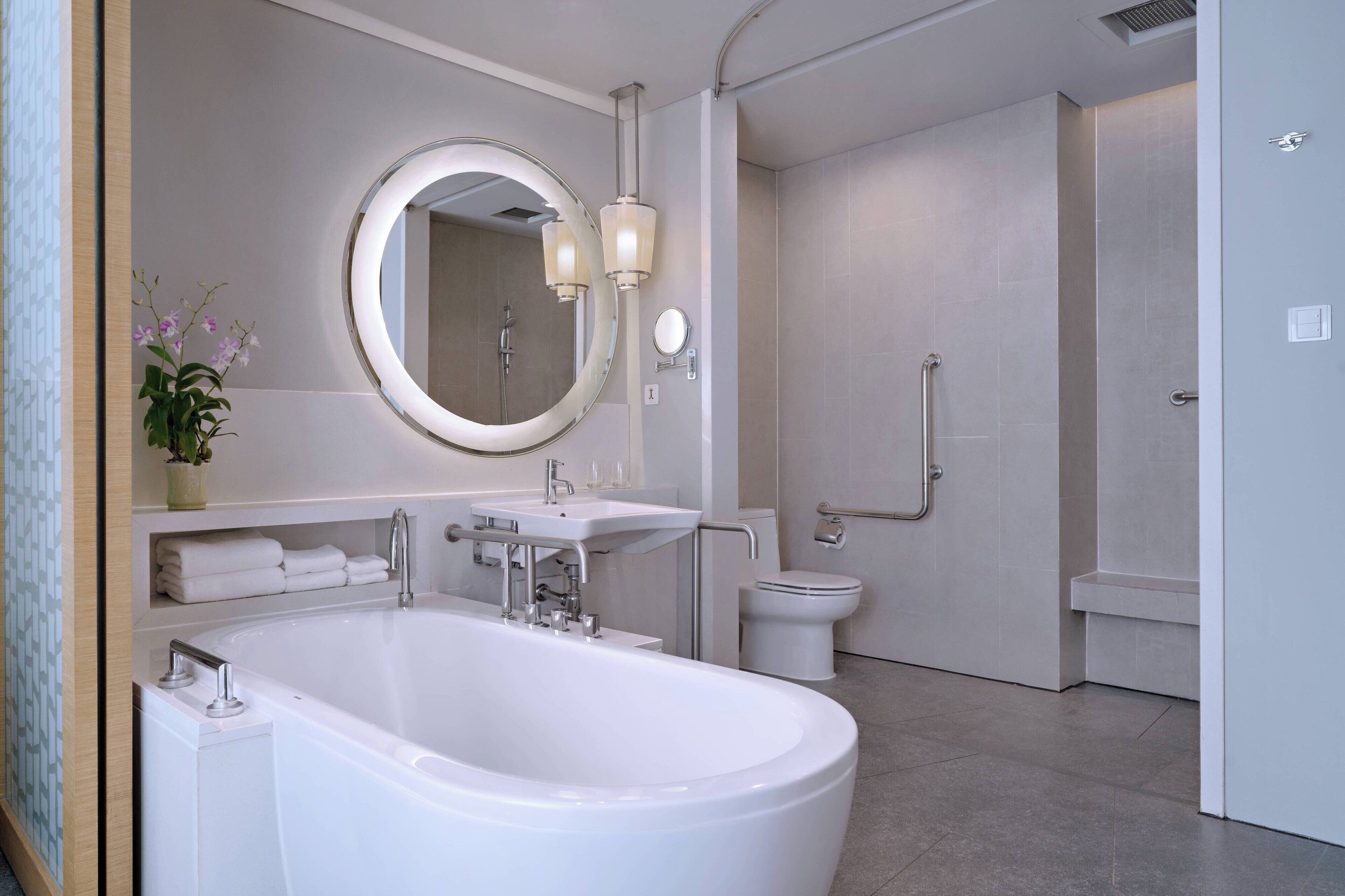 A modern bathroom with a freestanding bathtub, a round mirror, a toilet, and a shower area.