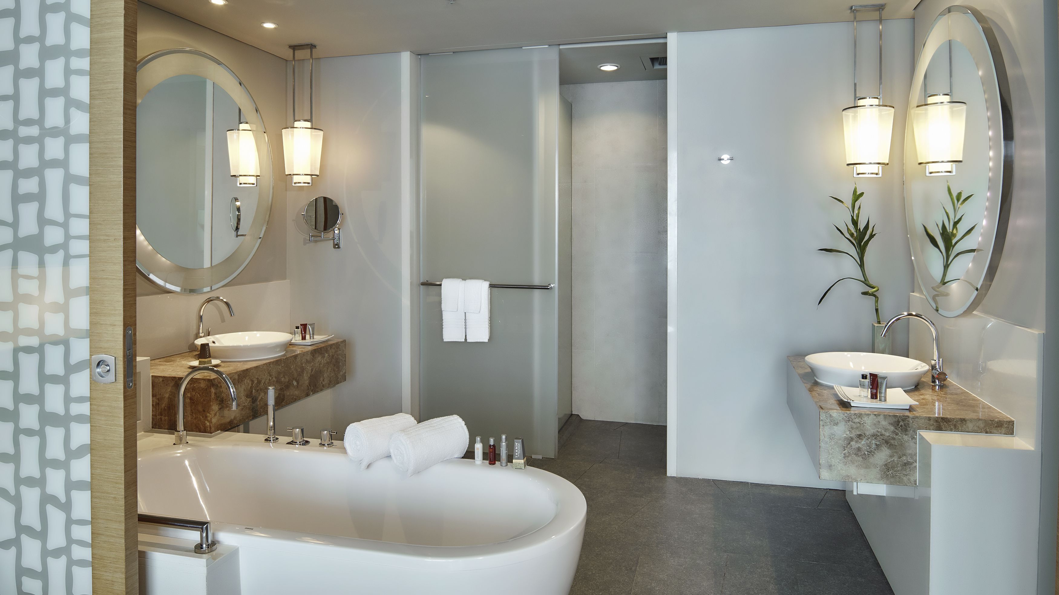 A modern bathroom with a freestanding bathtub, two sinks, and large mirrors.