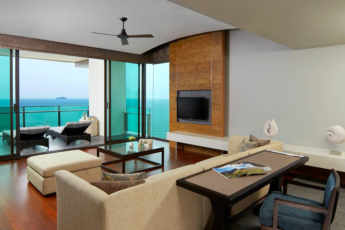 A modern living room with a large glass door leading to a balcony overlooking the sea.