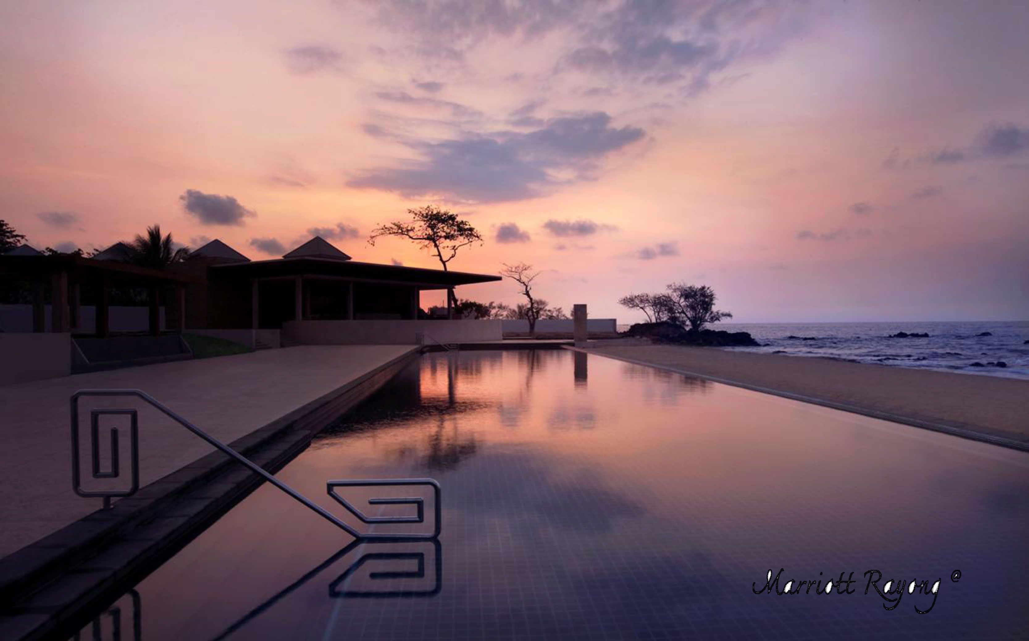 Un área de piscina tranquila con vista al atardecer, reflejando el cielo y la arquitectura circundante.