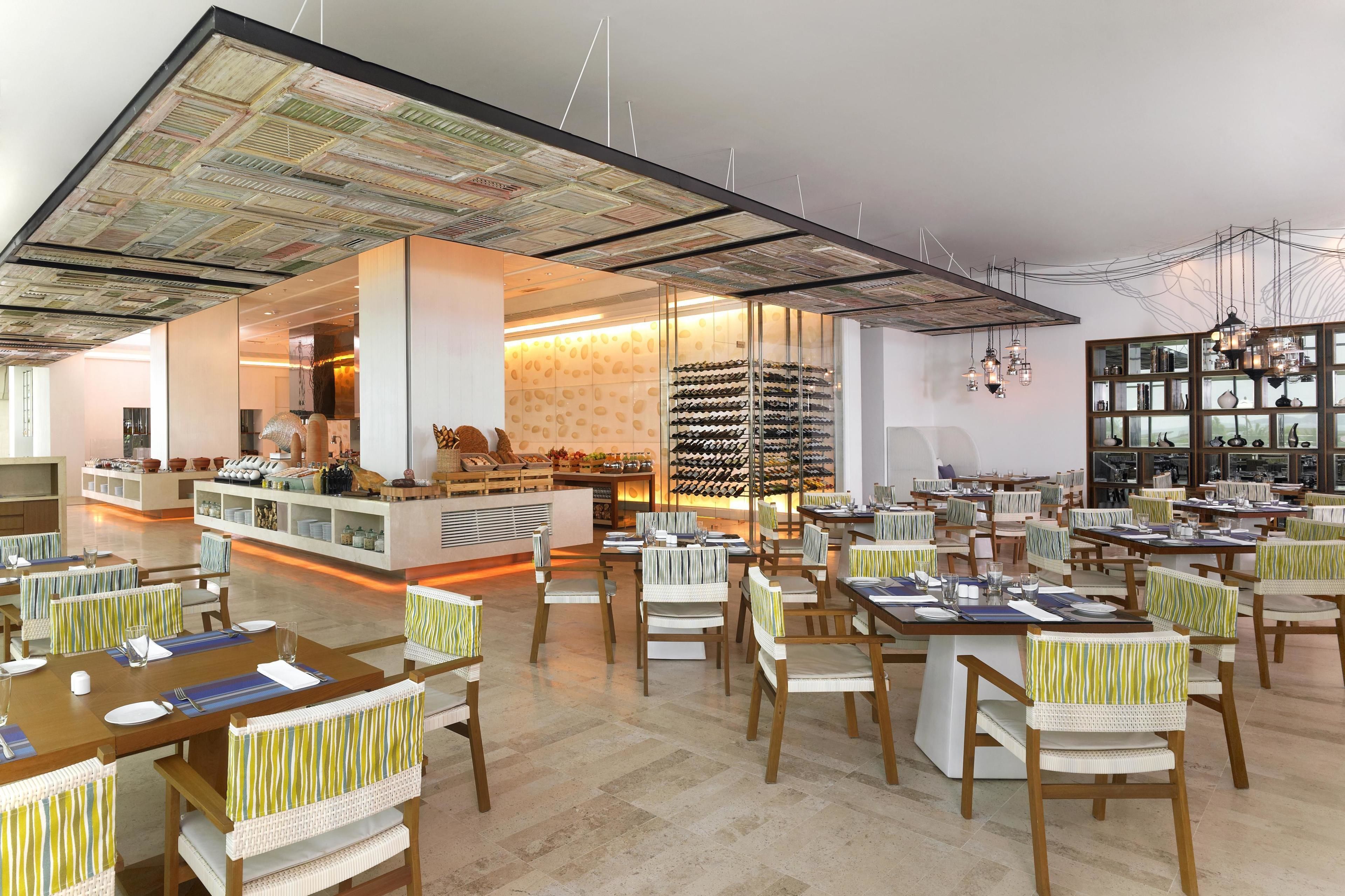 A spacious restaurant with multiple dining tables and chairs, a wine rack, and a kitchen area visible through a glass partition.