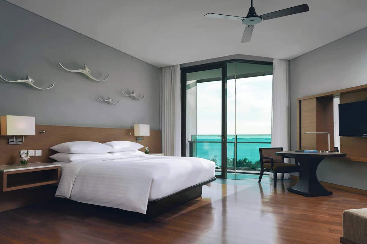 A modern hotel room with a large bed, bedside tables, a desk, and a view of the ocean.
